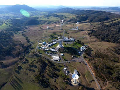 Aerial view of several white dish-like radio telescope antennas on a brown-green landscape