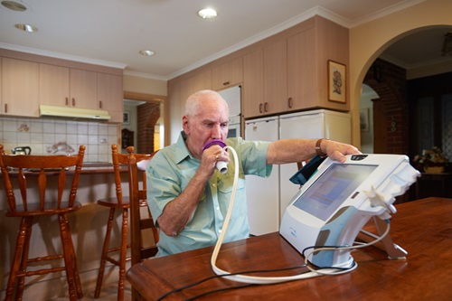 Man using the breathing apparatus of the home monitoring telehealth device.