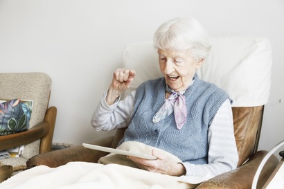 An elderly lady in a chair using a tablet device.