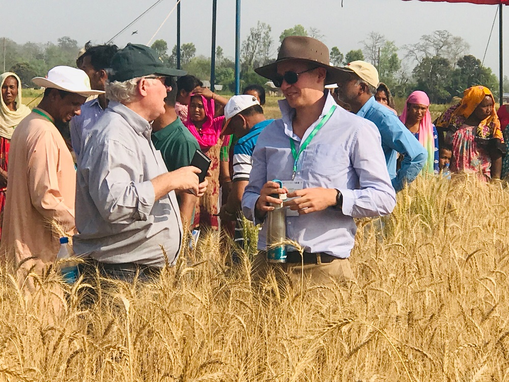 Group of people in a field of crops with two men talking in foreground 