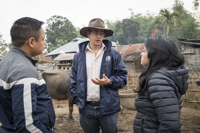 Three people talking with cow in background