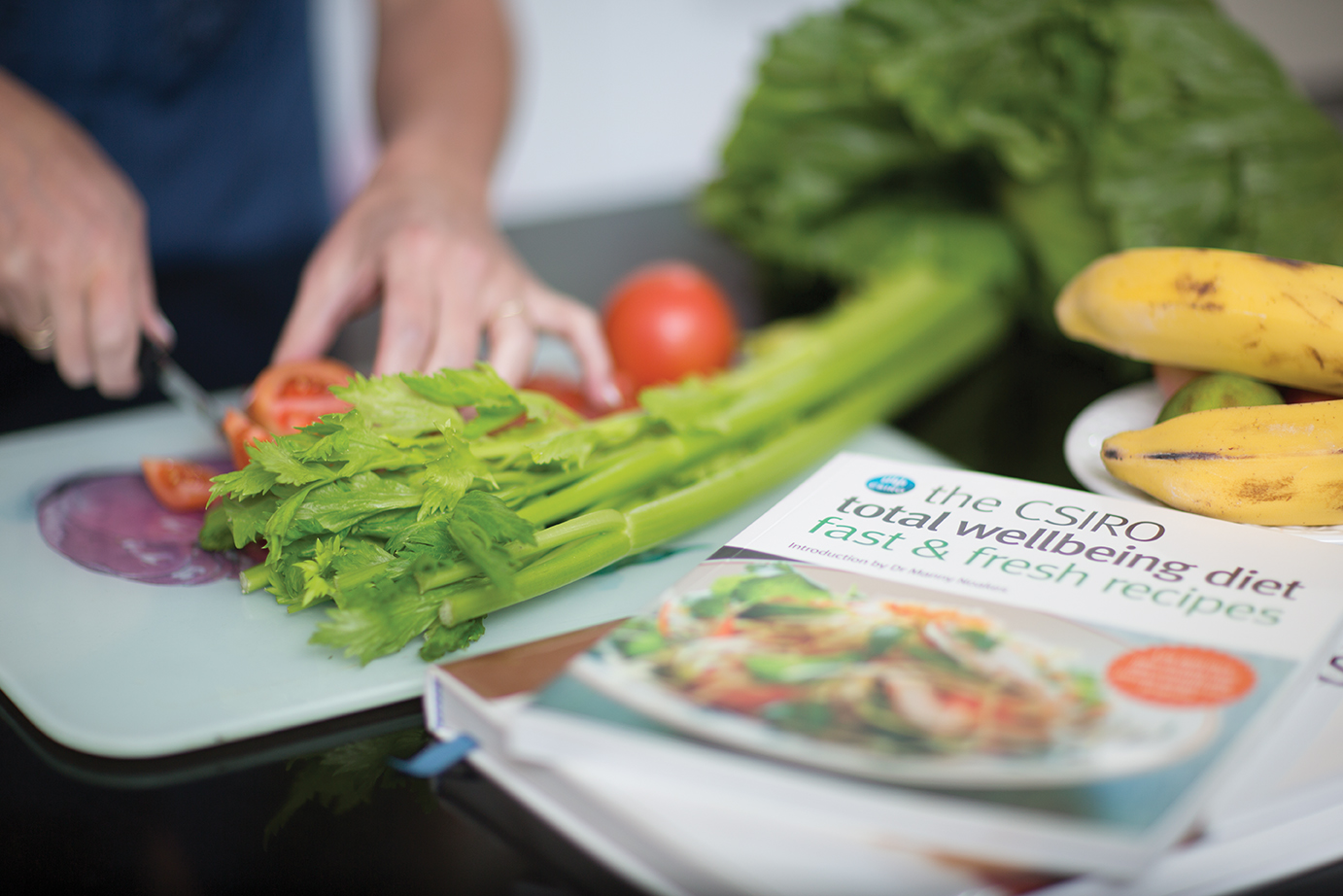 Hand chopping up salad veggies on a chopping board with the CSIRO Total Wellbeing Diet book in the foreground.