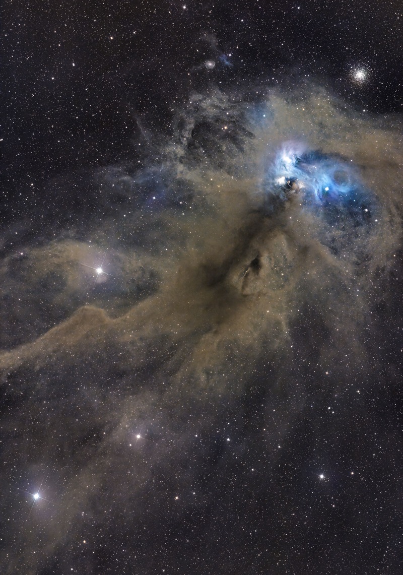 A background of stars with grey, brown wispy gas and dust cloud in the foreground. Towards the top right of the image there is an intense blue to white bubble of gas.