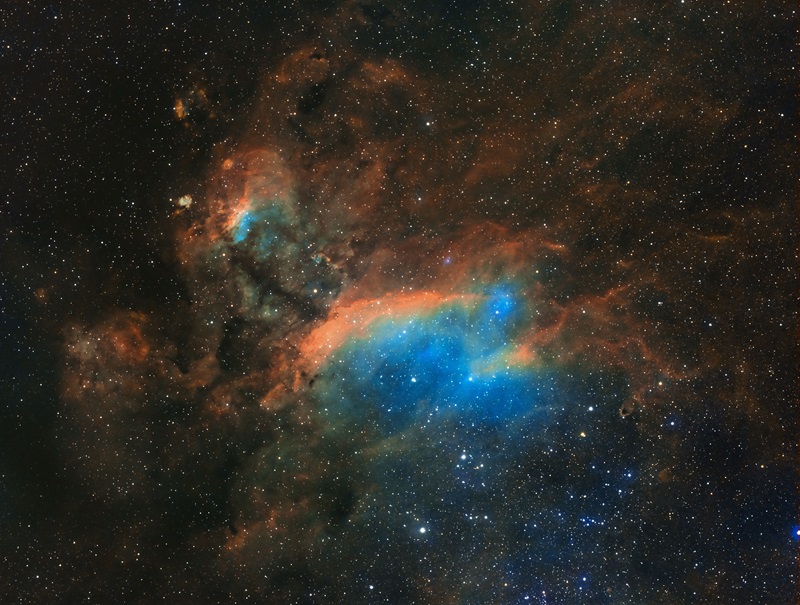 background star field with bright orange and blue clouds of gas in the foreground. 