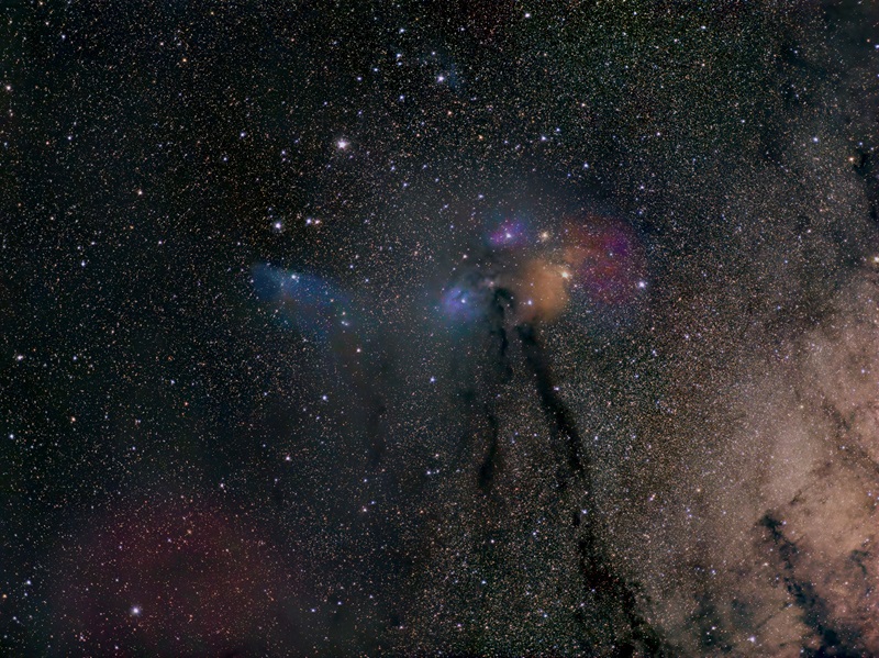 background of stars with distinct coloured gas clouds in blue, orange, red and purple in the centre of the image. 