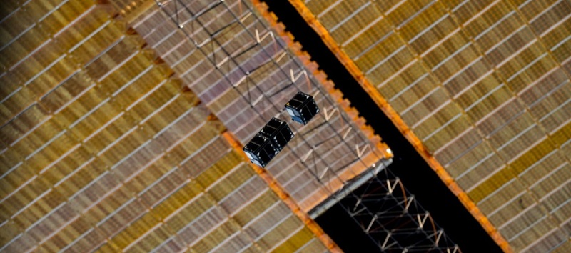 Three cube sats are visible against the backdrop of the International Space Station