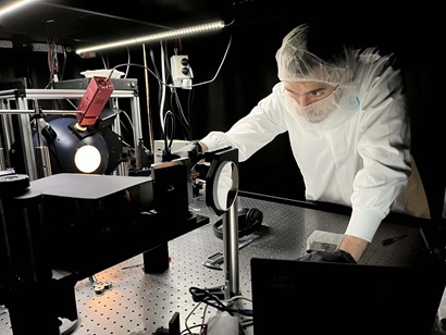 Researcher, Dr Joshua Pease wearing protective clothing leaning over working with laboratory equipment in CSIRO's Space Optics Lab.