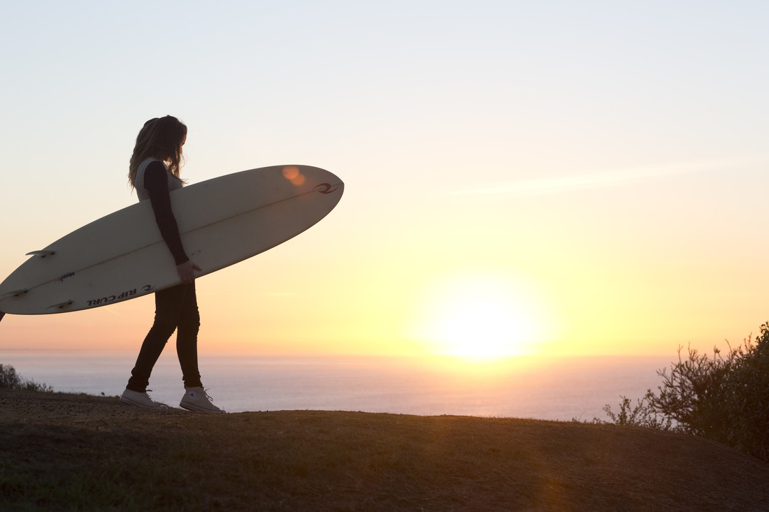 A woman holding a surfboard in front of the sunset