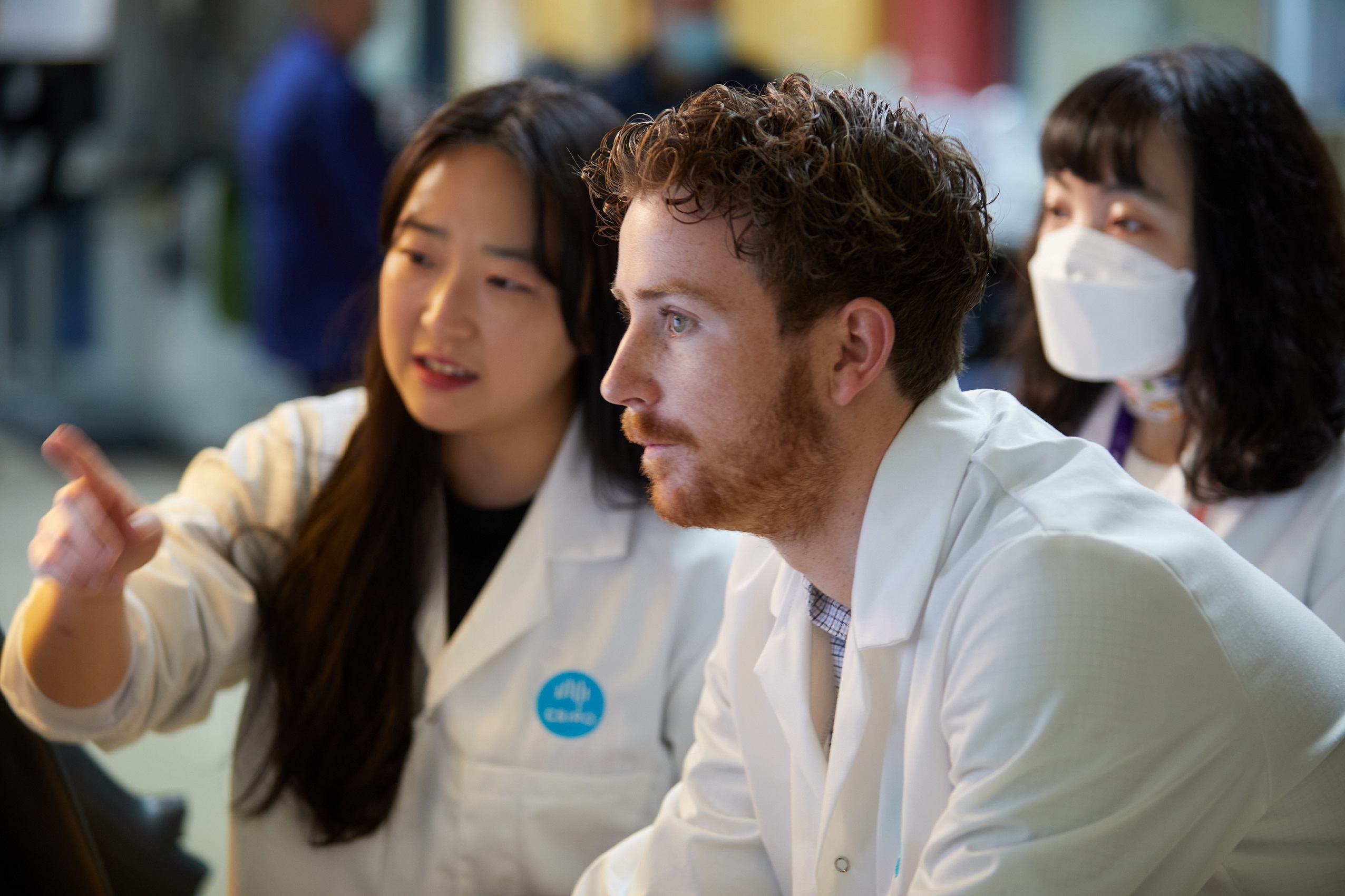 Two females and a male in lab coats looking at a screen