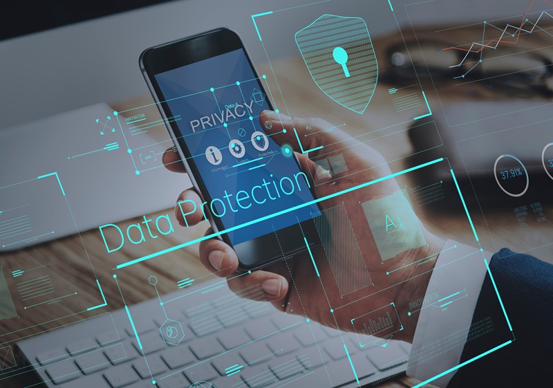 A phone is shown in someone's hand, with holographic images of a shield and lock, and the words data protection hovering in front of the screen.