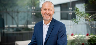 A portrait photo Dr Doug Hilton CSIRO Chief Executive sitting in front of slightly blurred background of plants in a garden. 