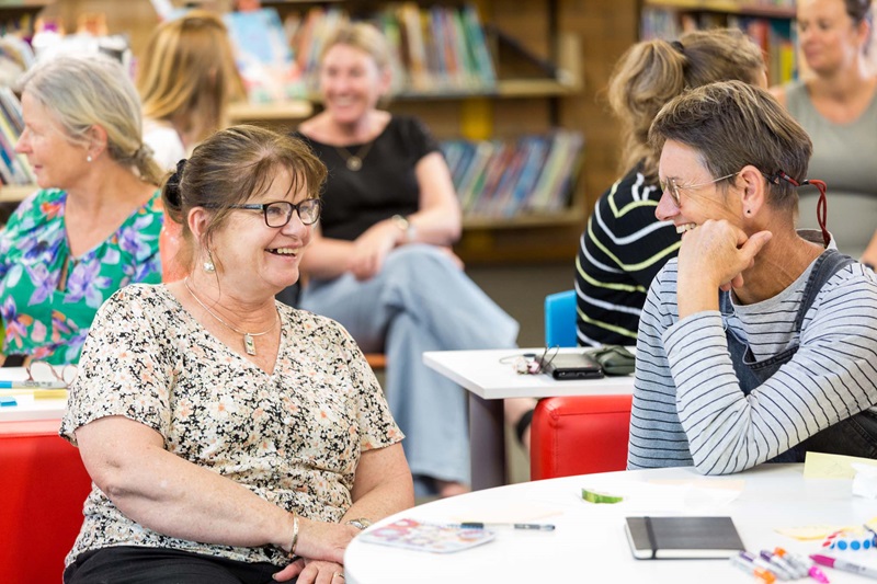 Two teachers talking at a networking event with more smiling teachers in the background.