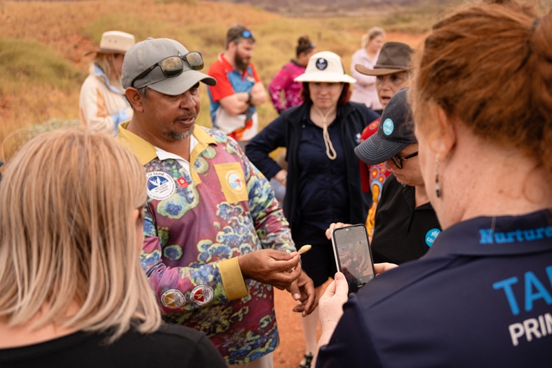 Indigenous man Clinton Walker shows local plant to group of teachers as they listen and take photographs