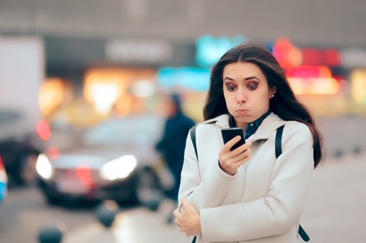 Woman standing on street looking at her phone with eyebrows raised