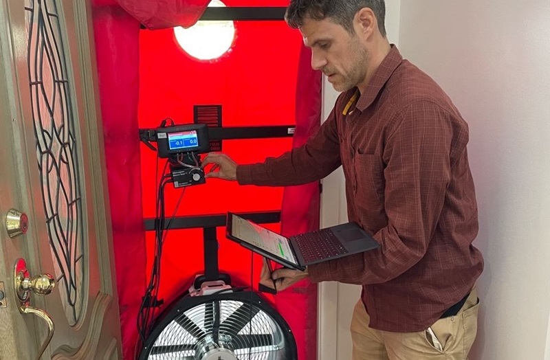 Man stands near door operating blower door test equipment