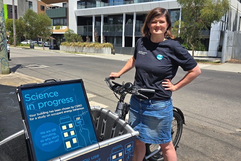 CSIRO energy research scientist Pippa Soccio stands in a street with a bike attached to a basket carrying sandwich boards.