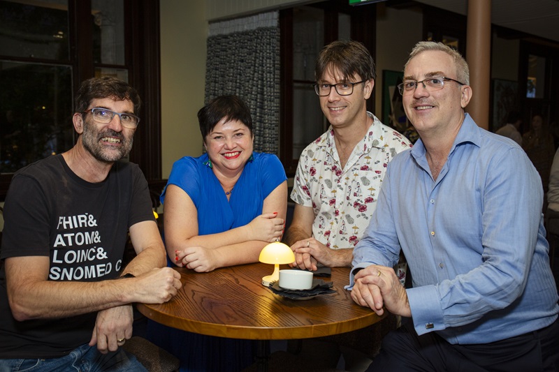 Four people leaning on a cafe table and looking at the camera