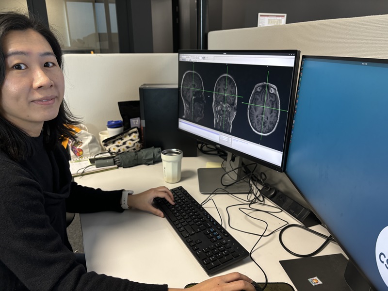 Woman with black hair works on a computer showing images of brains.