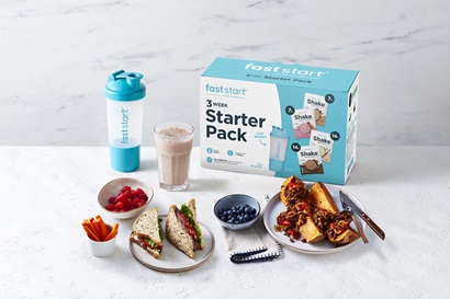 Fast Start meal replacement box sitting atop a counter with a shake in a glass surrounded by plates of food including blueberries and a sandwich