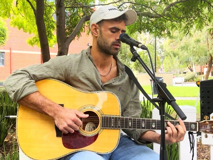 Jesse performs outdoors, playing an acoustic guitar and singing into a microphone