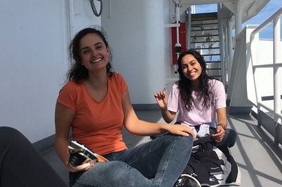 Two women sit on the deck of a ship and smiling.