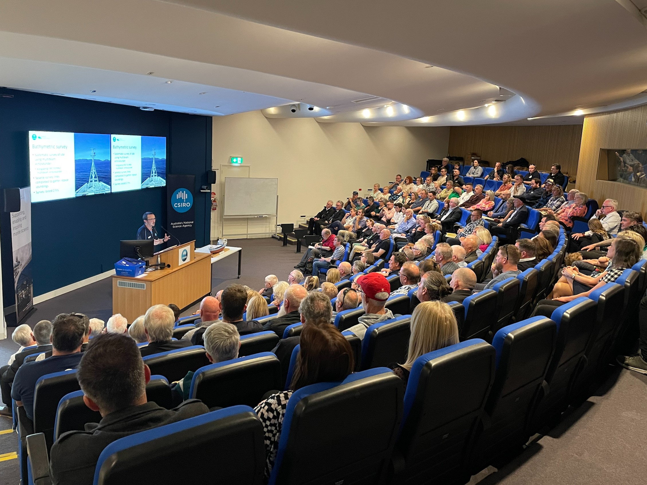 A person presenting to a large audience of people in an auditorium.