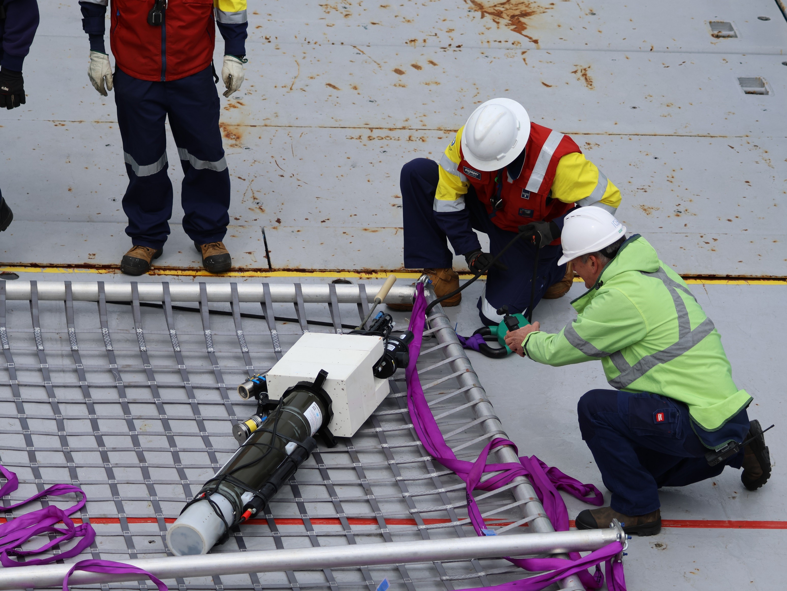 People on the deck of a ship look at a piece of scientific equipment that has just been recovered form the ocean.