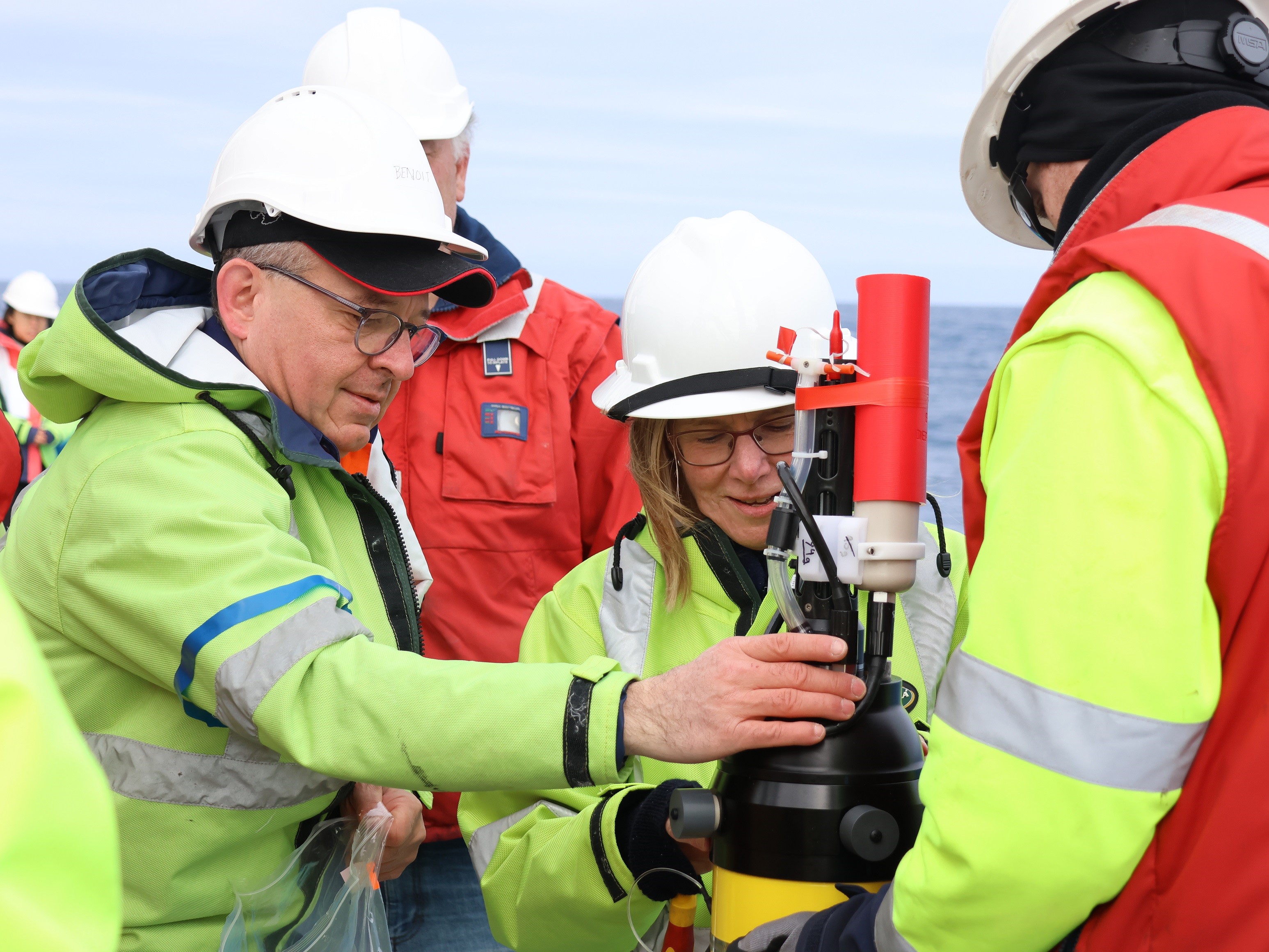 A group of people in hi-vis clothing and hard hats stand around a piece of scientific equipment.