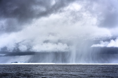 Grey clouds over the ocean with icebergs in the distance.