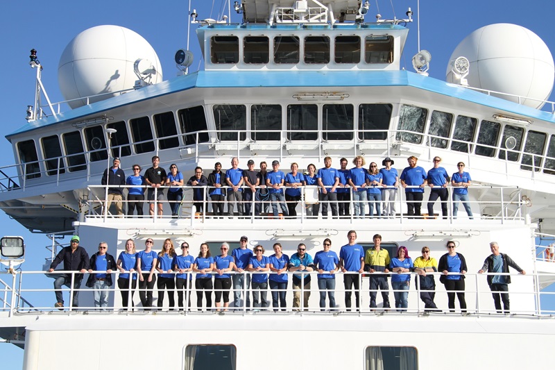 A group of people all wearing blue t-shirts standing on the deck of a large white ship.