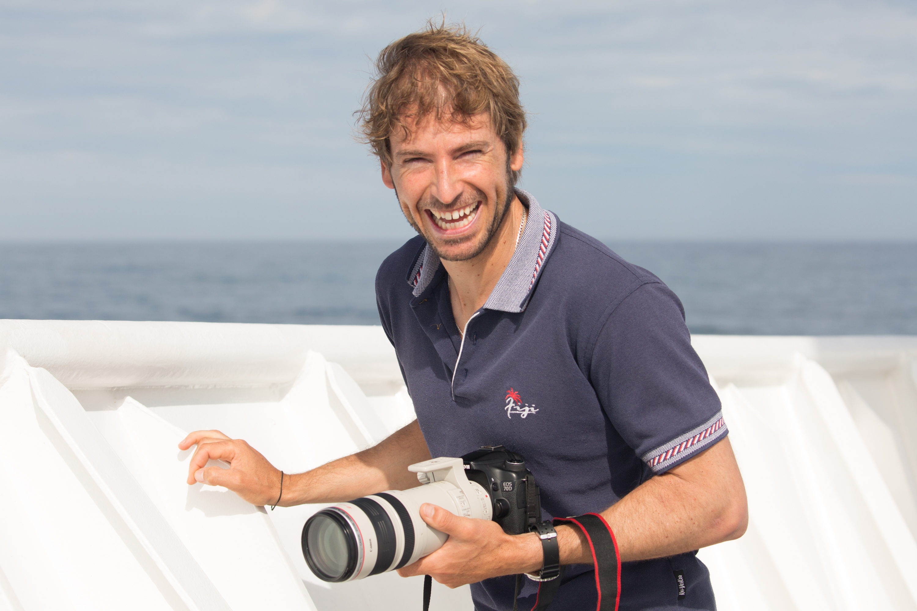 A young man holding a camera on the ship's deck.