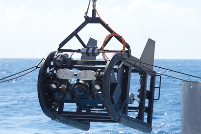 A piece of scientific equipment with cameras on it being lowered into the ocean.