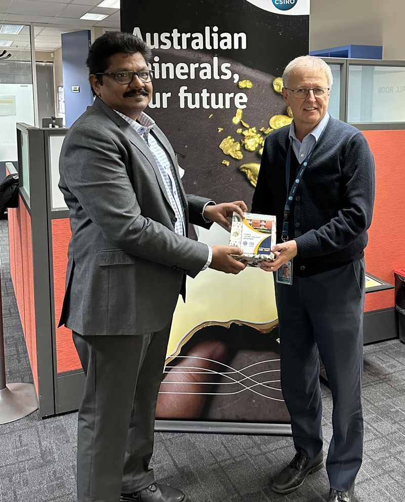 Two men, smiling and standing in front of a pull-up banner that says Australian minerals our future. The men appear to be in an office.