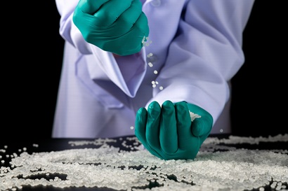 Scientist wearing green gloves working with polymer pellets