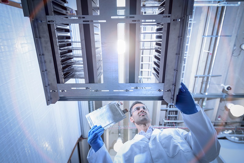 Scientist in a lab coat with lithium ion pouch cell manufacture machine in battery research facility, low angle view