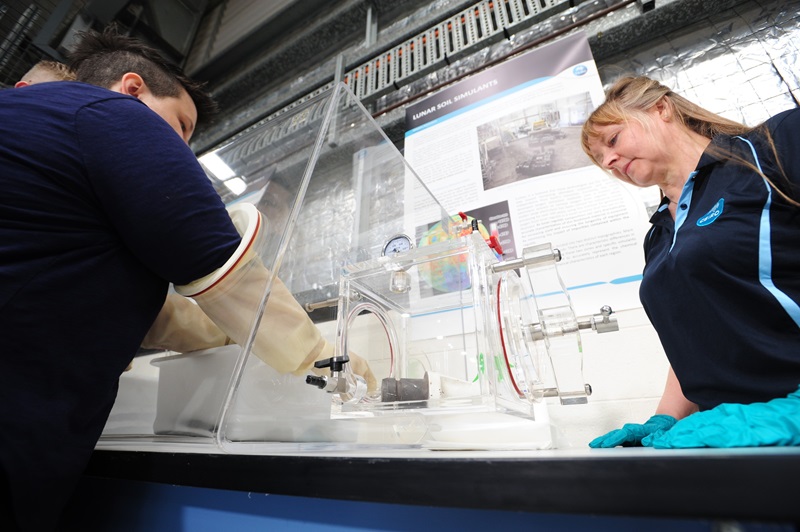 two people, including Dr Jane Hodgkinson in a CSIRO polo shirt, looking at a soil-like substance in a test box