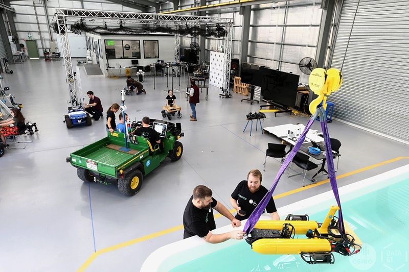 Pople  interacting with a variety of robots in a large room including a pool with an aquatic robots being lowered