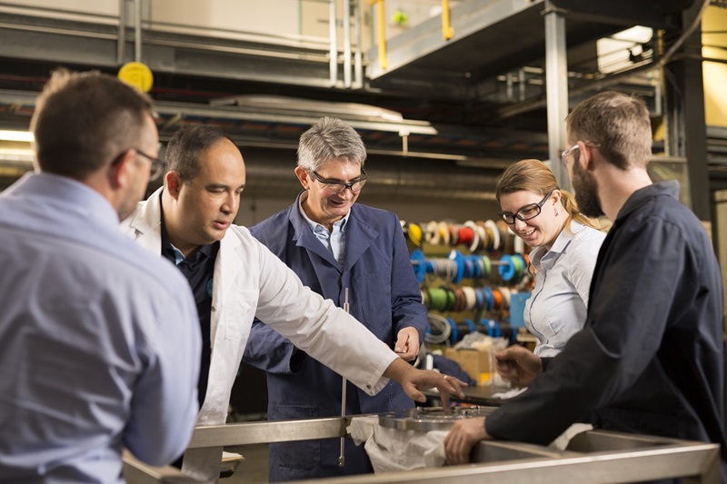 Group of five people looking at and touching circular metal object