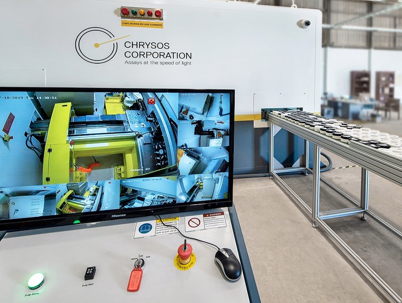 Computer monitoring showing Photon Assay machine workings with conveyor belt of samples in the background