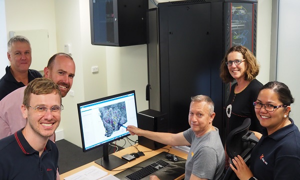 Four men and two women gathered around a central computer screen