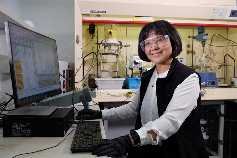 Female scientist wearing safety goggles sitiing in front of computer in lab