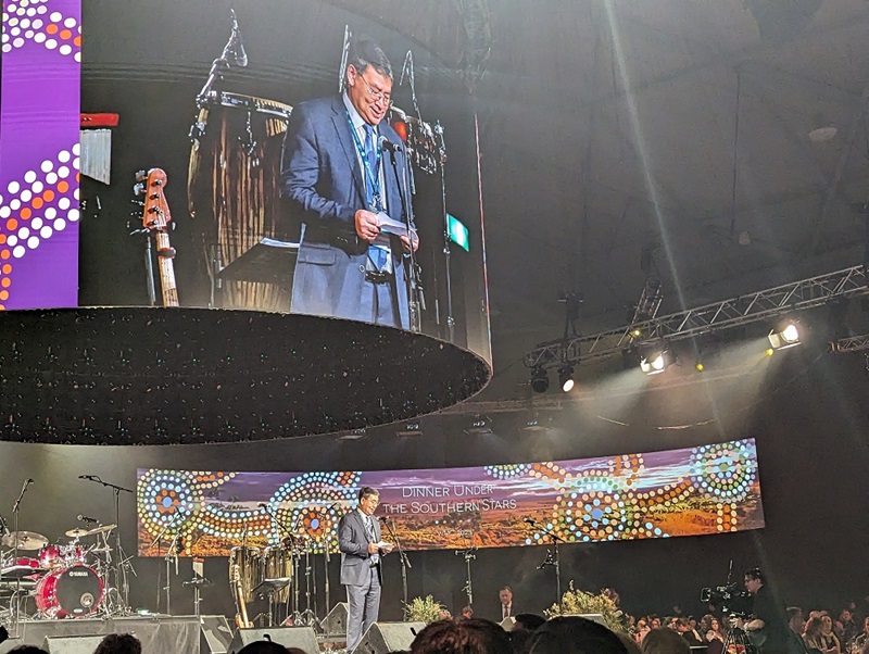 Man on stage projected larger on screen above stage