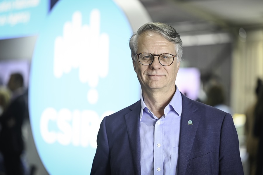 Dr Alex Held stands in front of a large CSIRO logo blurred in the background.