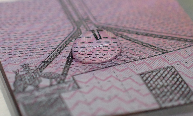 A droplet of liquid forming a circular mound in the middle of a small sqaure of cut Australian five dollar banknote.