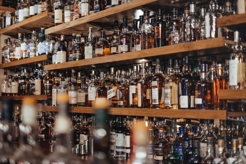 Bar with many bottles of alcohol arranged on different shelves. 