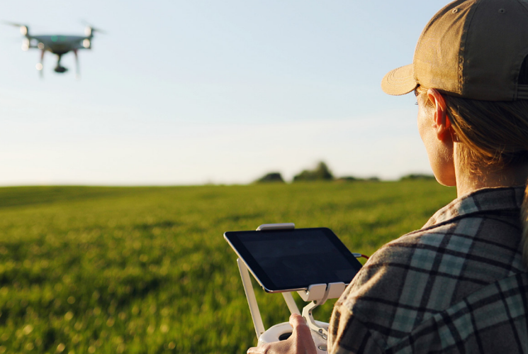 Person holding controller for drone as it flies across green pasture. 