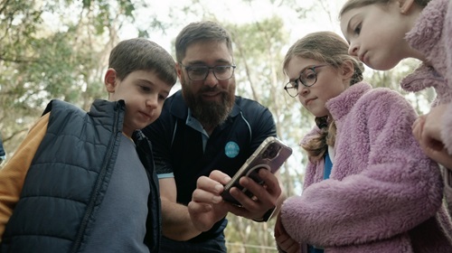 CSIRO National koala Monitoring Program research lead Dr Andrew Hoskins shows Jonathan Wright,10, and twins Grace and Vera McAulay, 9, how to use the Koala Spotter app. Ormiston Queensland. July 9, 2024.