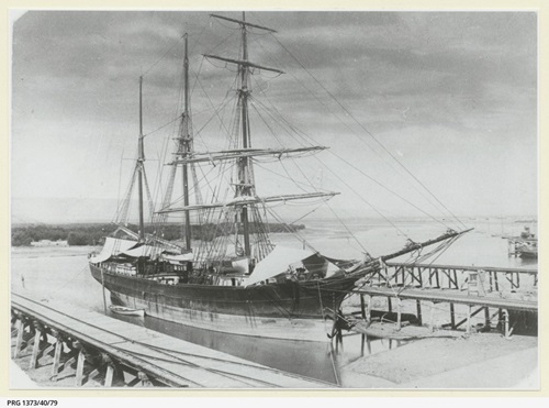 A black and white image of a sailing ship at a wharf.