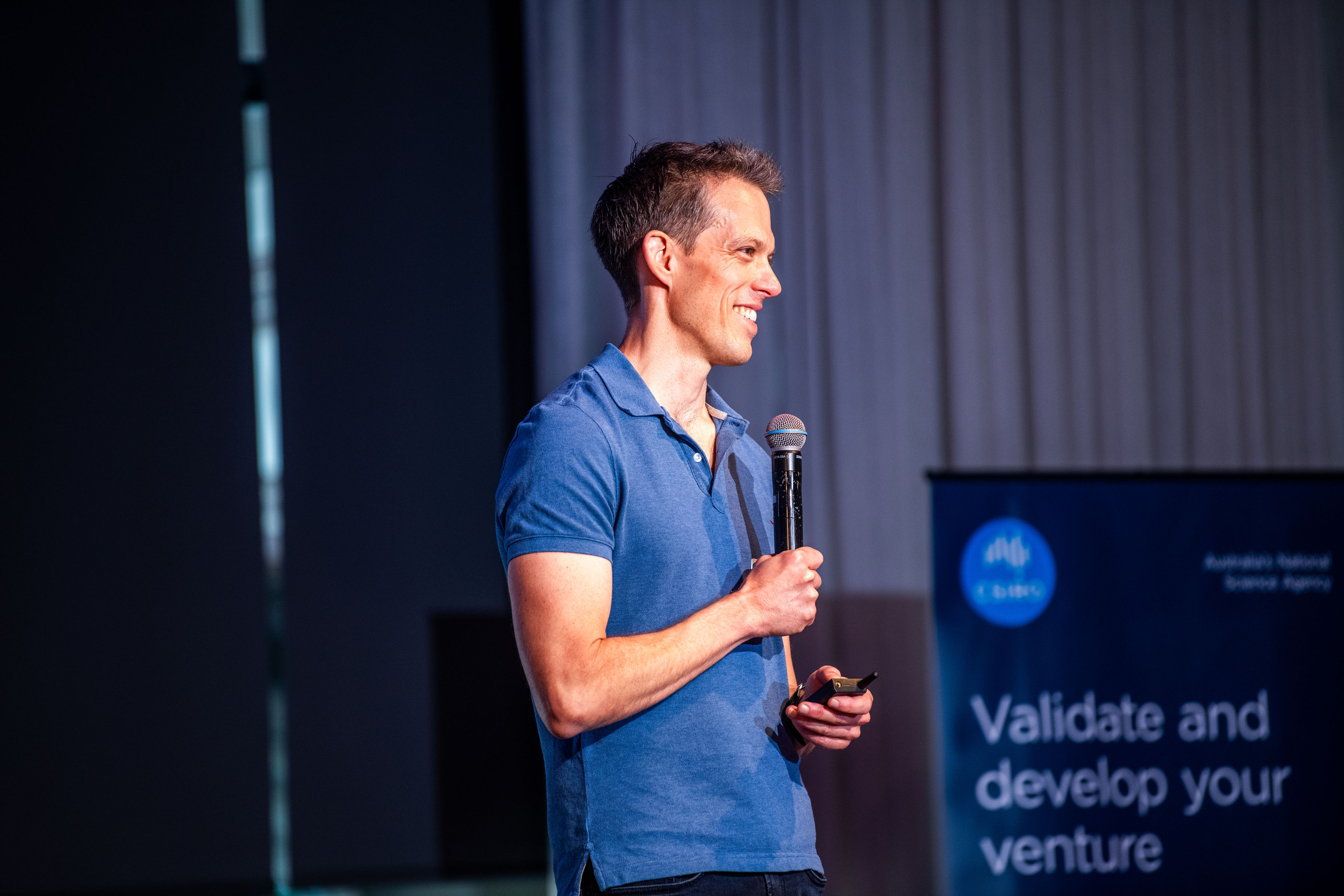 A man wearing a blue shirt addresses an audience, confidently giving a speech from a podium