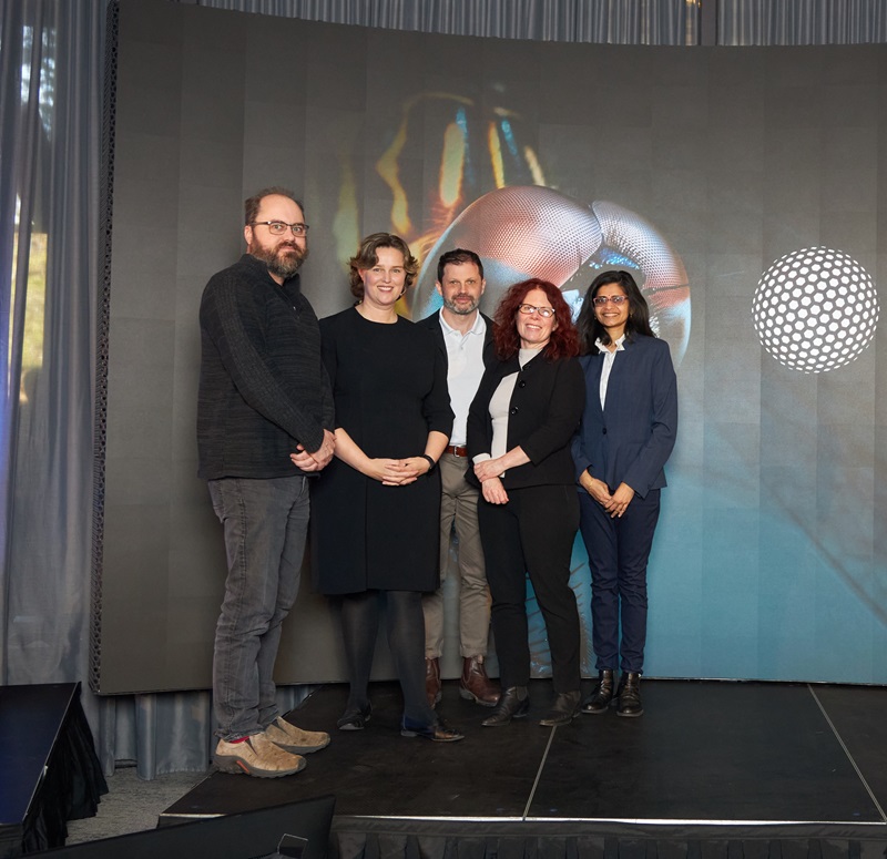 Five people standing on a stage in front of a large screen